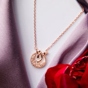 A rose gold wreath pendant chain in silver material, displayed on a mannequin wearing a grey coat and a red flower is visible in the foreground.
